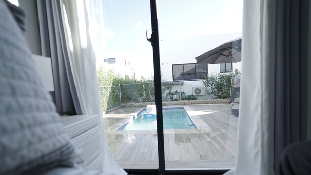 A bedroom with a view of an outdoor swimming pool and a person standing by the pool.