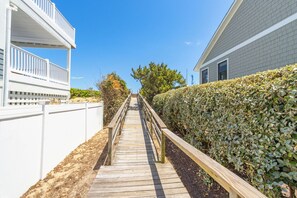 A wooden pathway leading to a building with a white exterior and a balcony.