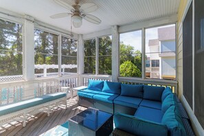 A covered porch with a white railing, a blue sofa, a glass coffee table, and a ceiling fan. - Charming pet-friendly home w/ pool & family-friendly community amenities! (Corolla)