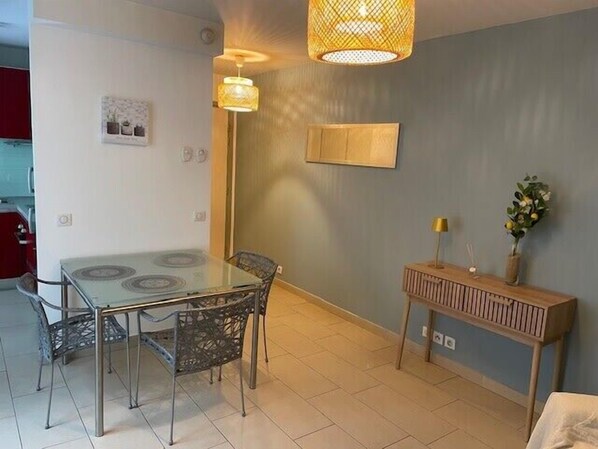 Un coin repas avec une table en verre et des chaises en métal, un buffet en bois surmonté d’une lampe, et un tableau accroché au mur.