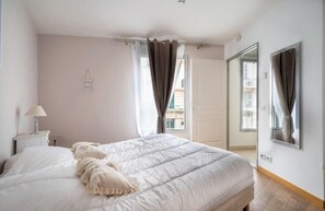 Une chambre avec un grand lit, une table de chevet avec une lampe, une fenêtre avec des rideaux et un miroir sur le mur.