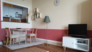 Un soggiorno con pavimento in legno, un tavolino da caffè color petrolio, un mobile TV bianco, un tavolo da pranzo con sedie e una lampada da terra.