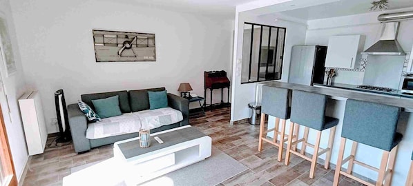 Una sala de estar moderna con un sofá, una mesa de centro y un área de cocina con un taburete de bar y una estufa.
