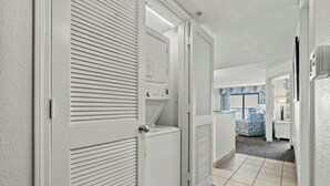 Corredor com portas brancas, chão ladrilhado e vista para um quarto com cama e janela.