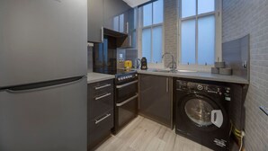 A compact kitchen with a built-in washing machine, a refrigerator, and a window providing natural light. - Guild Street Apartment | Grampian Lettings Ltd (Aberdeen)