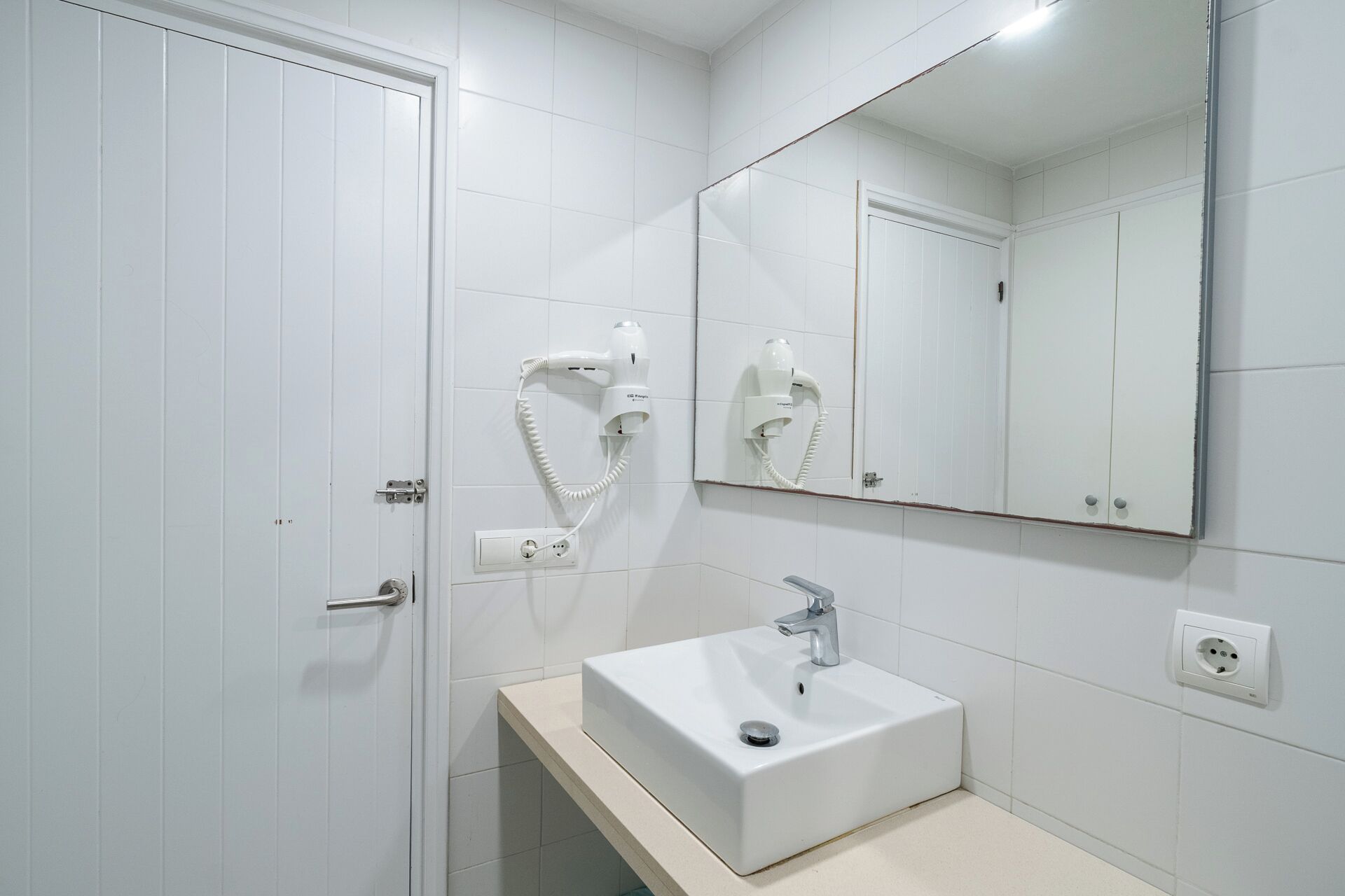Un bagno con un lavandino bianco, uno specchio e un asciugacapelli montato a parete.