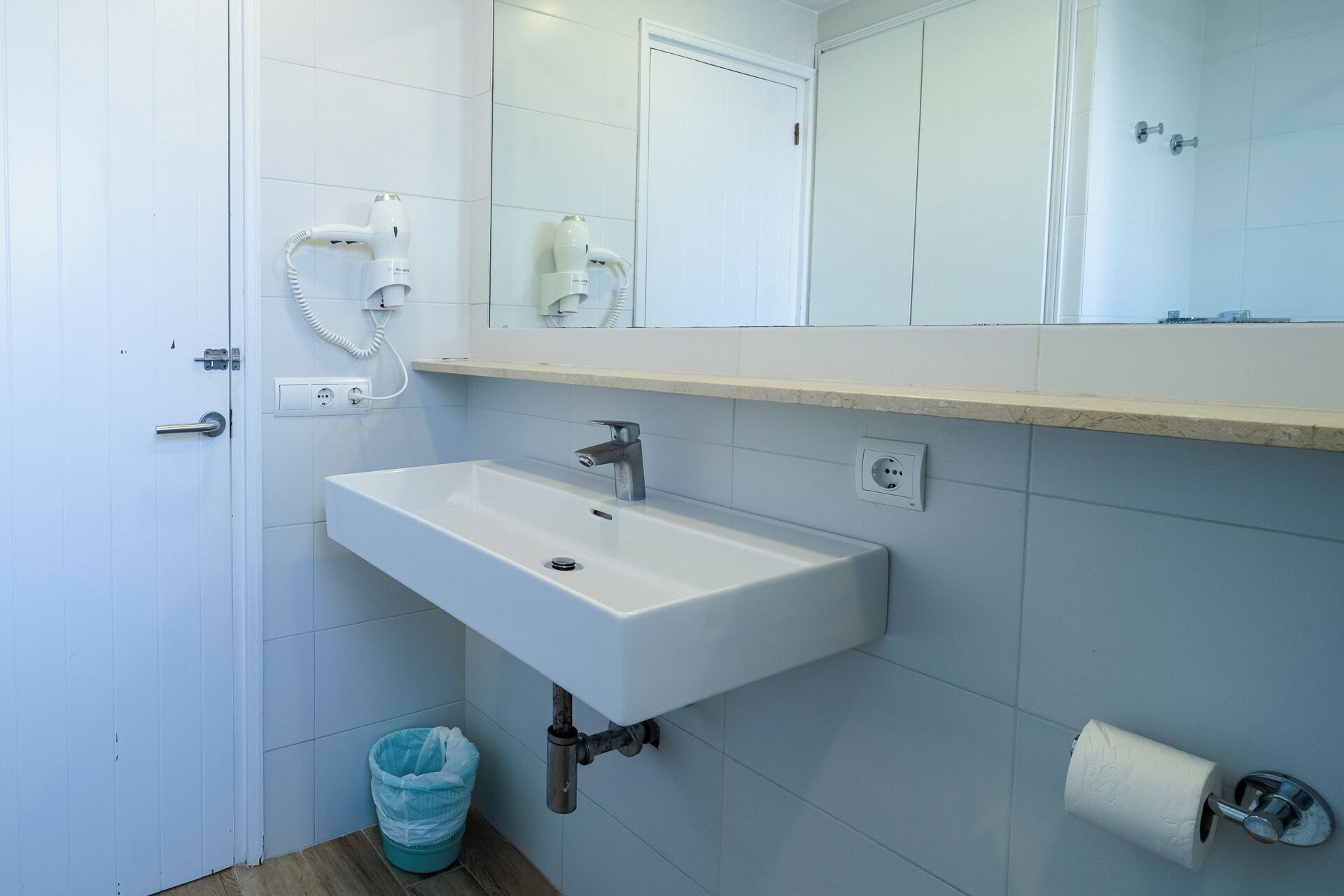 Une salle de bain avec un lavabo blanc, un miroir et un distributeur de serviettes.