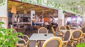 Un restaurant doté de mobilier en osier, de plantes suspendues et d’un comptoir bien visible.