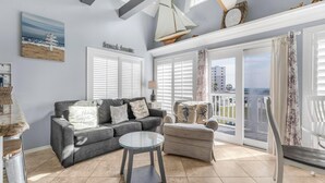 Sala de estar con un sofá gris, una mesa de centro redonda de cristal y un sillón gris. Hay una ventana grande con contraventanas blancas y vistas a la ciudad.