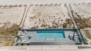 Eine Vogelperspektive eines Hotels am Strand mit Swimmingpool, Liegestühlen und einem eingezäunten Strandbereich.