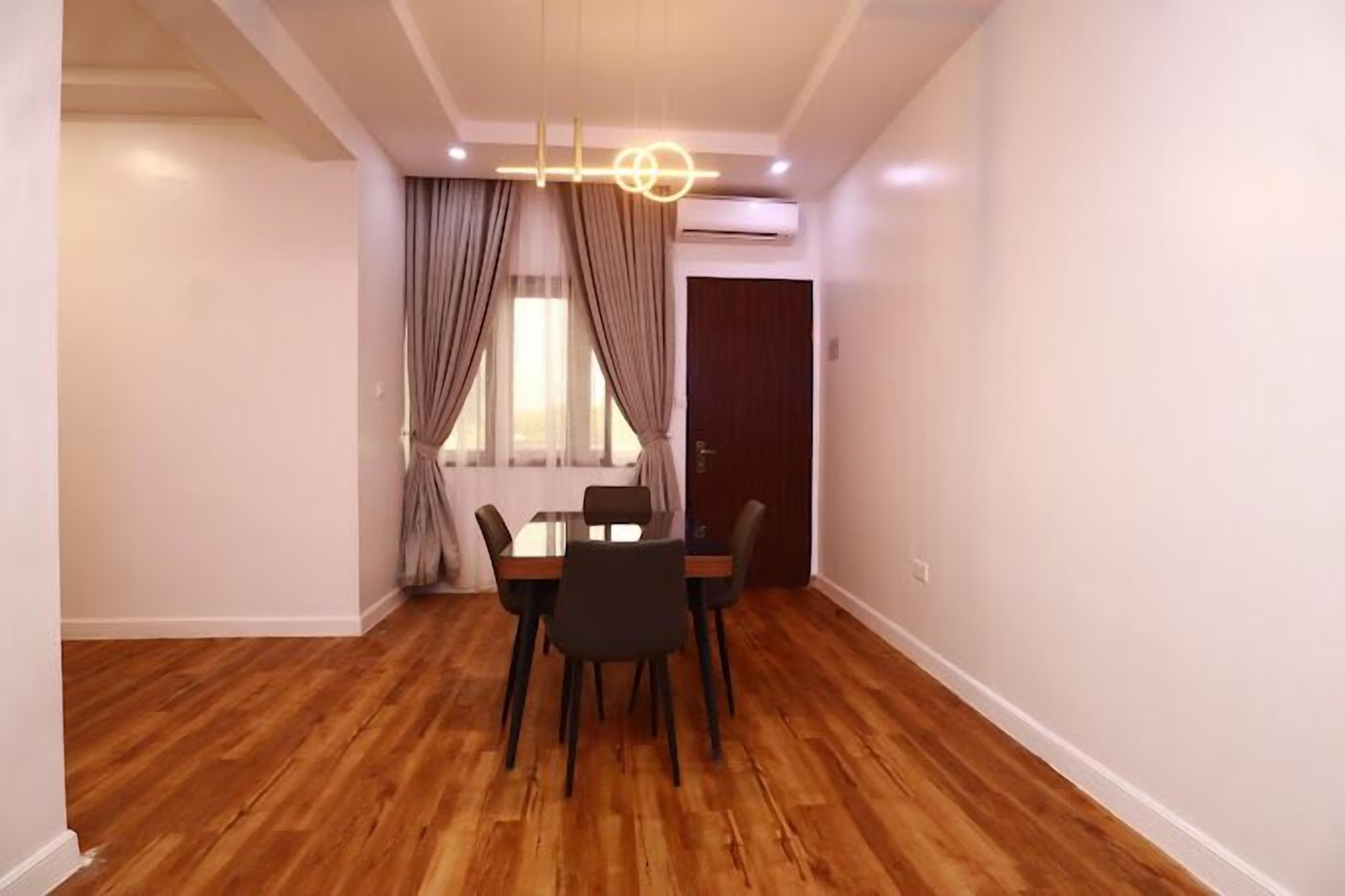 A dining area with a wooden table and chairs, a chandelier, and a window with curtains.