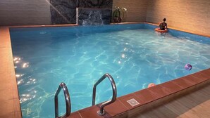 Une piscine intérieure à l’eau claire, avec un mur en pierre et un plancher en bois.