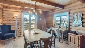 A wooden cabin interior with a dining table, chairs, a lamp, and a ski-themed sign.