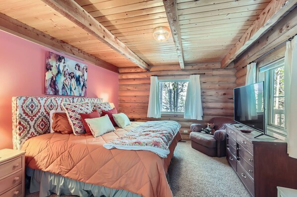 Ein gemütliches Schlafzimmer in einer Blockhütte mit einem großen Bett, einem Fernseher und einem Fenster mit Vorhängen.