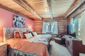 A cozy log cabin bedroom with a large bed, a TV, and a window with curtains. - Valley View Vistas - Dog-Friendly Cozy Retreat w/ VIEWS! (Nederland)