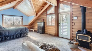 A cozy attic bedroom with a bed, dresser, and a wood-burning stove.