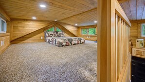 A cozy attic bedroom with a sloped ceiling, a bed with a patterned bedspread, and a view of trees through a window. - The Bear Cave tiny cabin experience*3 cabins in 1* (Broken Bow)