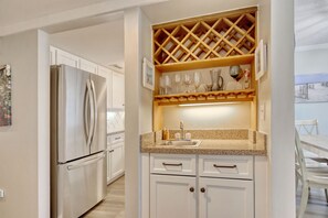 A kitchen with white cabinets, a stainless steel refrigerator, a granite countertop, a wine rack, and a sink.