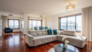 Amplia sala de estar con sofá modular, una mesa de centro y un comedor con sillas. Amplias ventanas ofrecen vistas de la ciudad.