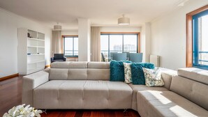 Una sala moderna con un sofá seccional, una estantería blanca y un ventanal con vista a la ciudad.