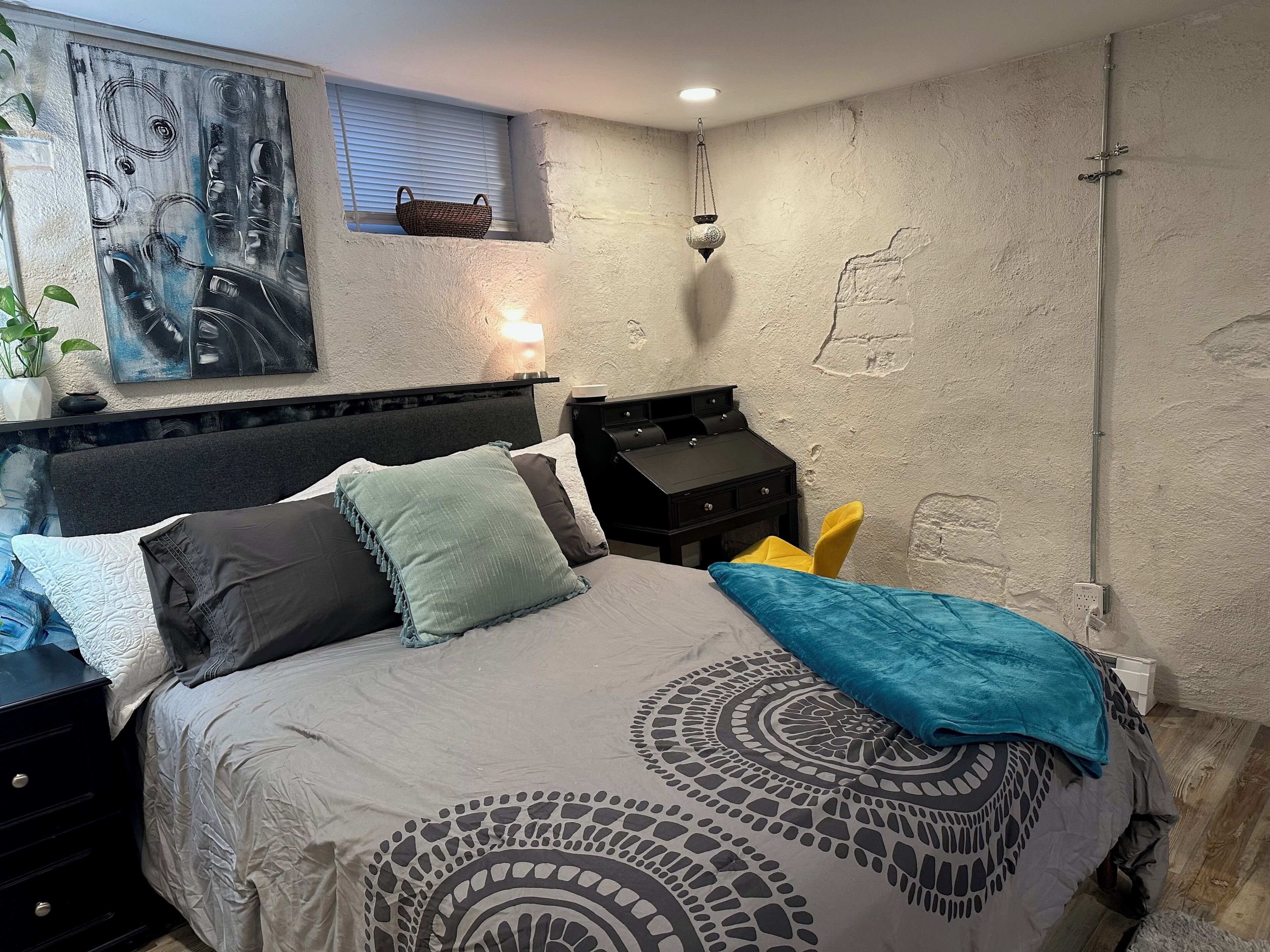 Een slaapkamer met een bed, nachtkastjes, een lamp, een wanddecoratie en een raam met zonwering.