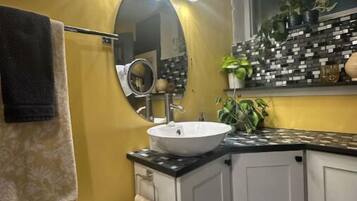Une salle de bain avec un lavabo blanc, des toilettes et un miroir. Il y a des lampes au-dessus du miroir et une fenêtre avec des plantes sur le rebord.