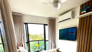 Une chambre à coucher avec un lit, un ventilateur de plafond, une télévision et une fenêtre avec des rideaux.