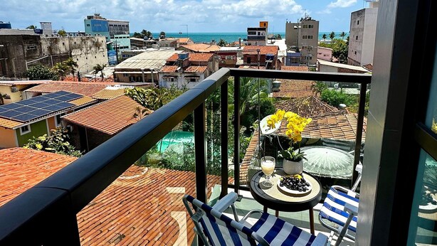Un balcon avec une table, des chaises et une vue sur le paysage urbain et l’océan.