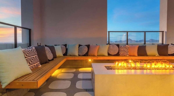 Un área de estar moderna con una chimenea, asientos con cojines estampados y vistas amplias a través de grandes ventanales.