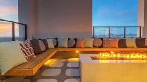 A modern lounge area with a long bench, patterned cushions, a fire feature, and a view of the mountains. - Boulevard Stays Modern Highrise STU Sky Pool, Gym 05 (Phoenix)
