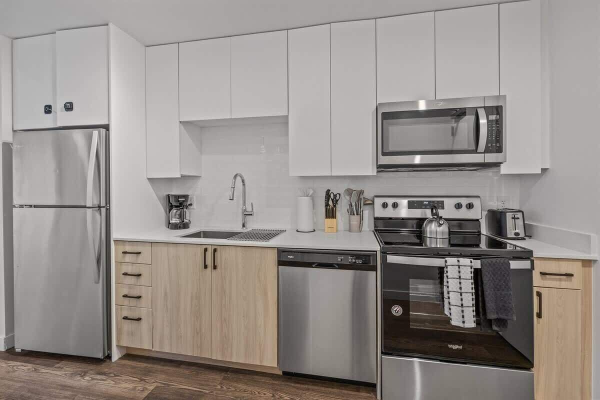 A modern kitchen with stainless steel appliances, white cabinetry, and a wooden countertop.