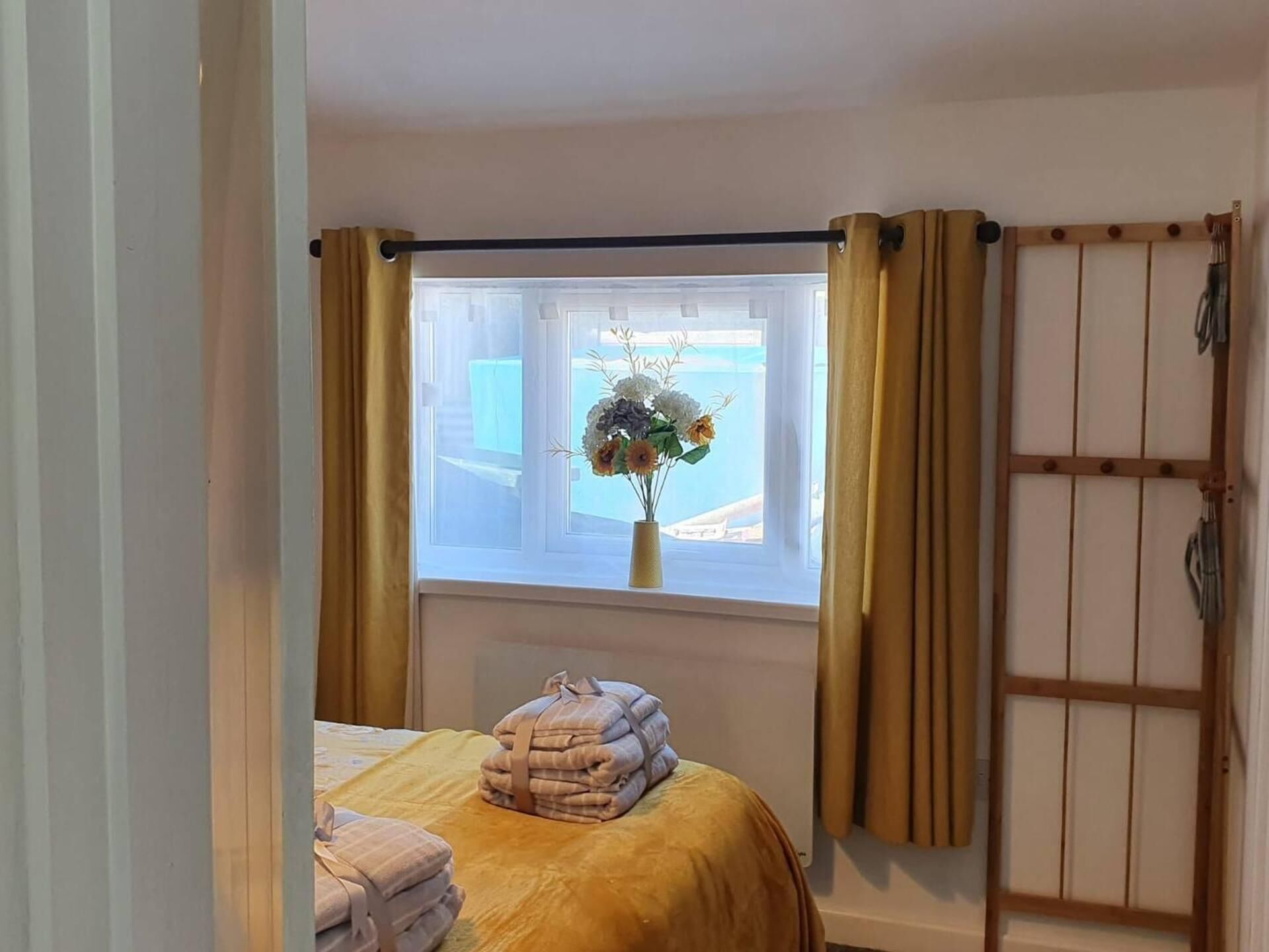 A bedroom with a bed, a window with curtains, a view of the outside, and a towel stack.