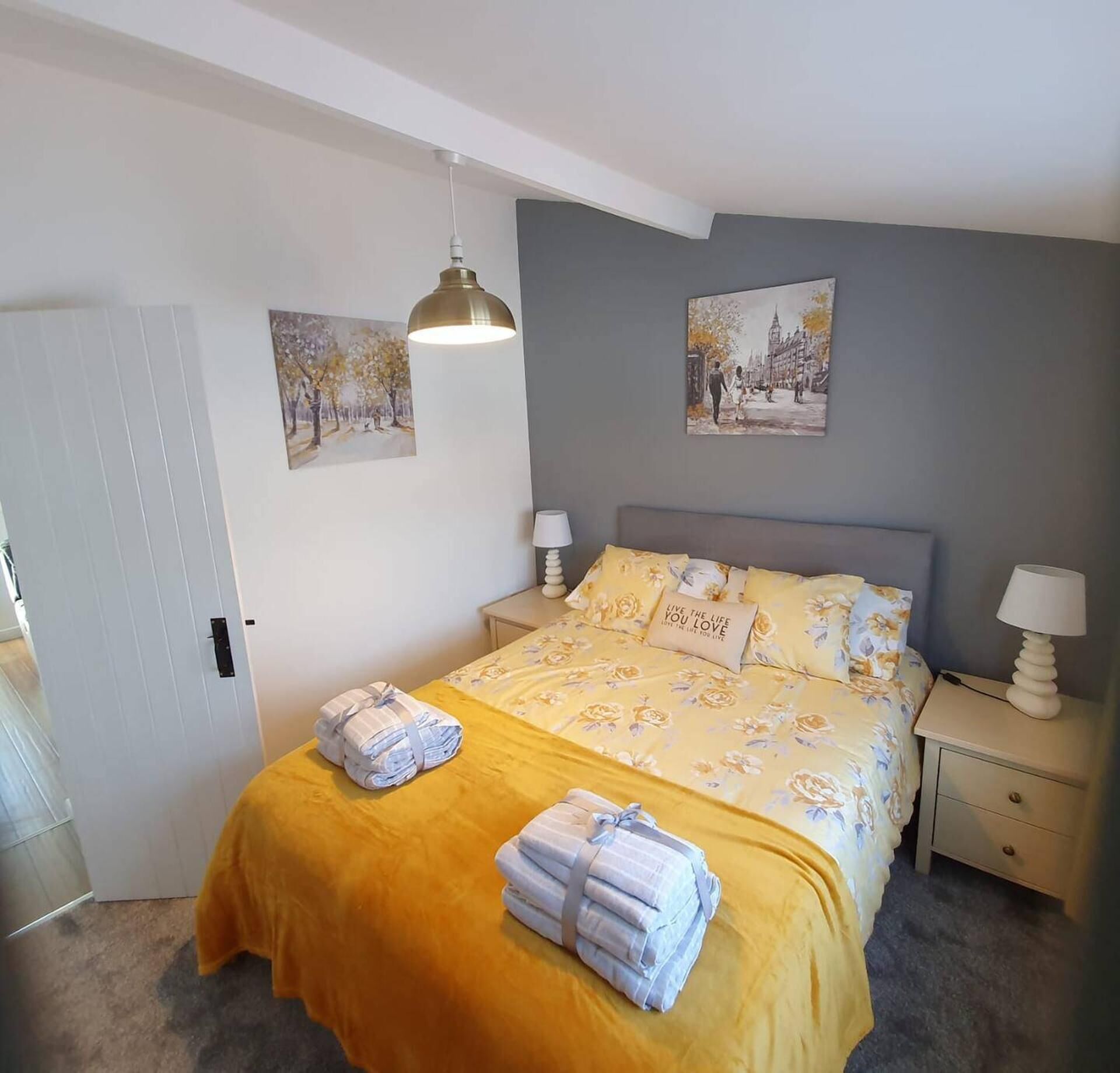 A bedroom with a bed, two nightstands, a bedside lamp, a door, and two wall-mounted paintings.