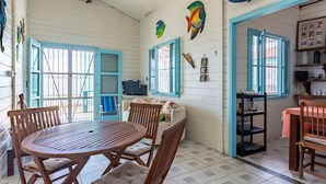 A room with a wooden table and chairs, a sofa, and a window with blue shutters. - Casa Beira Mar enseada dos Corais-SH098D (Cabo de Santo Agostinho)