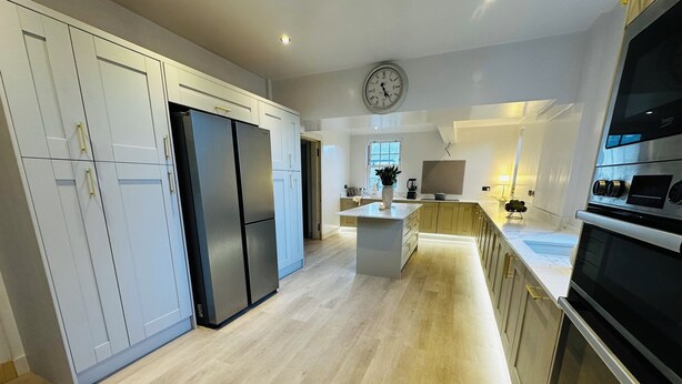Eine moderne Küche mit weißen Schränken, einem Edelstahl-Kühlschrank, einer Kochinsel mit Spüle und einem eingebauten Backofen.