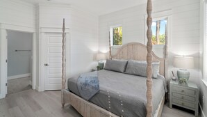 Ein Schlafzimmer mit Himmelbett, Nachttisch mit Lampe und Fenster mit Blick auf Bäume.