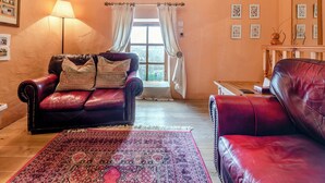 Un salon chaleureux avec un canapé en cuir rouge, un tapis à motifs et une grande fenêtre agrémentée de rideaux.