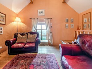 A cozy living room with a red leather sofa, a patterned rug, and a large window with curtains. - 2 bedroom accommodation in Llanwenog, near Llanybydder (Llanwenog, near Llanybydder)