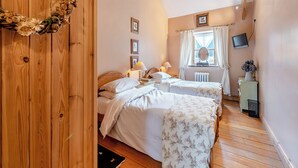 Une chambre confortable avec deux lits, un plancher en bois, une fenêtre avec des rideaux, un radiateur et un téléviseur fixé au mur.
