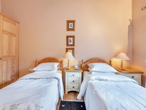 Camera da letto con due letti singoli, testiere in legno, comodini con lampade, un piano di appoggio e un armadio.