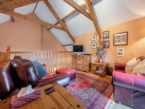 A cozy living room with a high ceiling, wooden beams, a television, a wooden dresser, a red sofa, and a patterned rug.