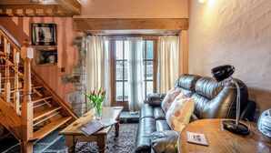 Un salon chaleureux avec un escalier, un canapé en cuir, une table basse en bois et un tableau accroché au mur.