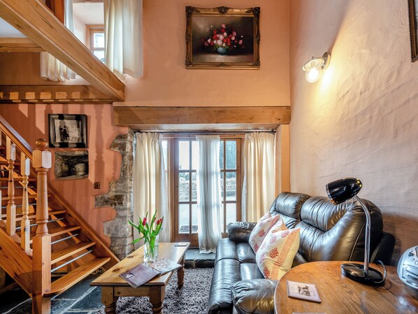 A cozy living room with a staircase, a leather sofa, a wooden coffee table, and a painting on the wall.
