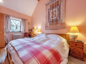 A bedroom with a bed, bedside lamps, a dresser, a window with curtains, and a wall tapestry.