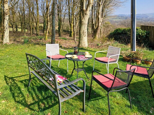 A garden with a table and four chairs, surrounded by trees and a view of the countryside.