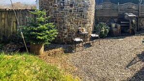 Une tour en pierre avec une clôture en bois, une petite table avec des chaises et une plante en pot.