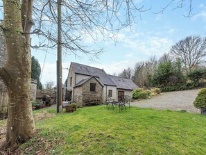 Una casa in pietra con tetto spiovente, un prato e un vialetto di ghiaia che conduce all'ingresso.