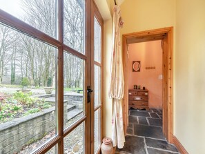 A room with a large window, a wooden door, a stone staircase, and a small wooden dresser.