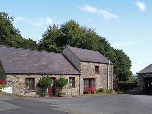 A stone building with a sloped roof, a red door, and a window with a red frame.