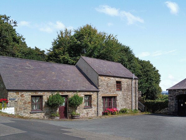 A stone building with a sloped roof, a red door, and a window with a red frame.